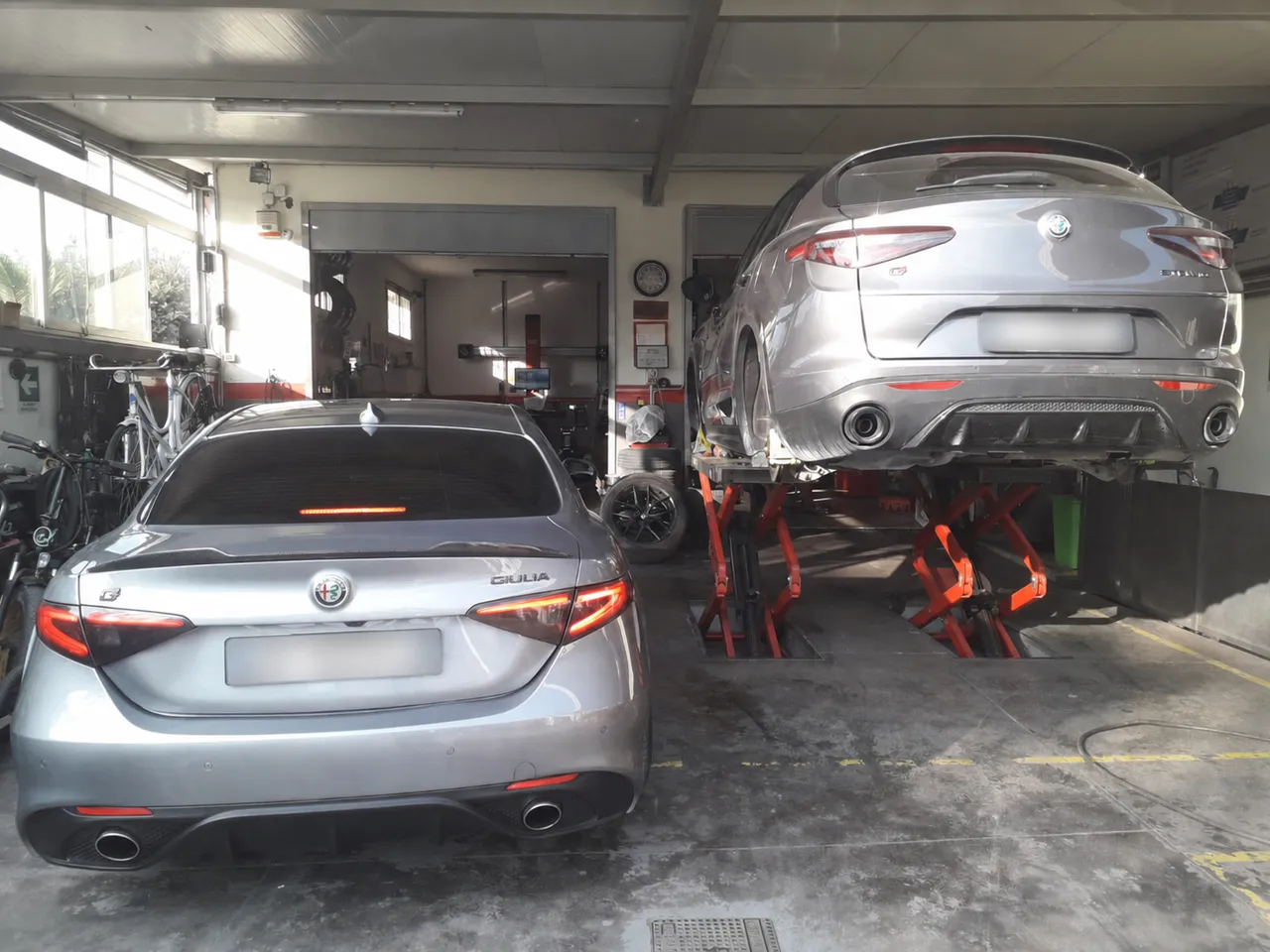 Alfa in officina, una a terra e una sul ponte: ordine e spazio per lavorare senza urti.