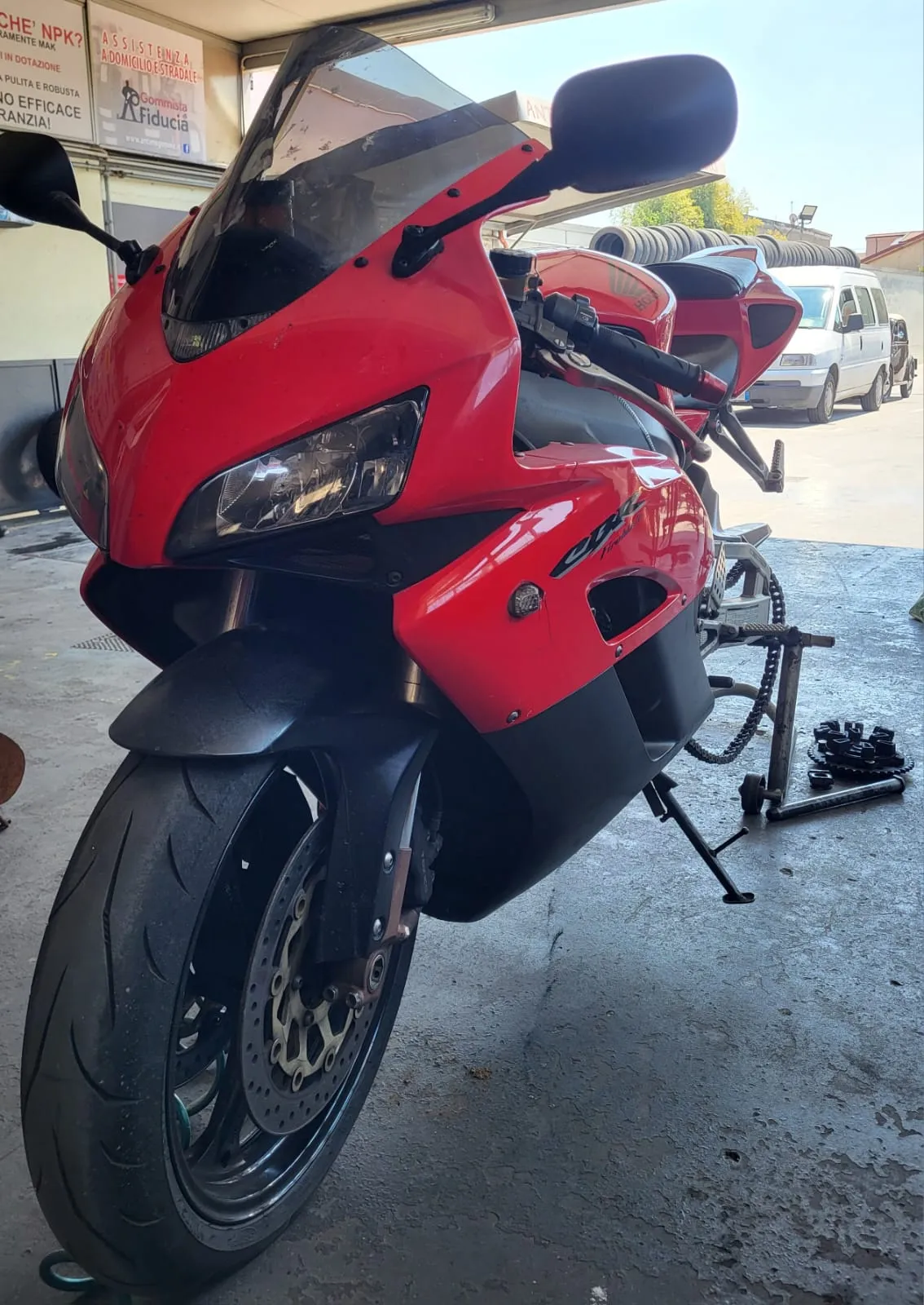 Moto sportiva sul cavalletto con la ruota posteriore smontata: gomma, catena e corona si controllano insieme.