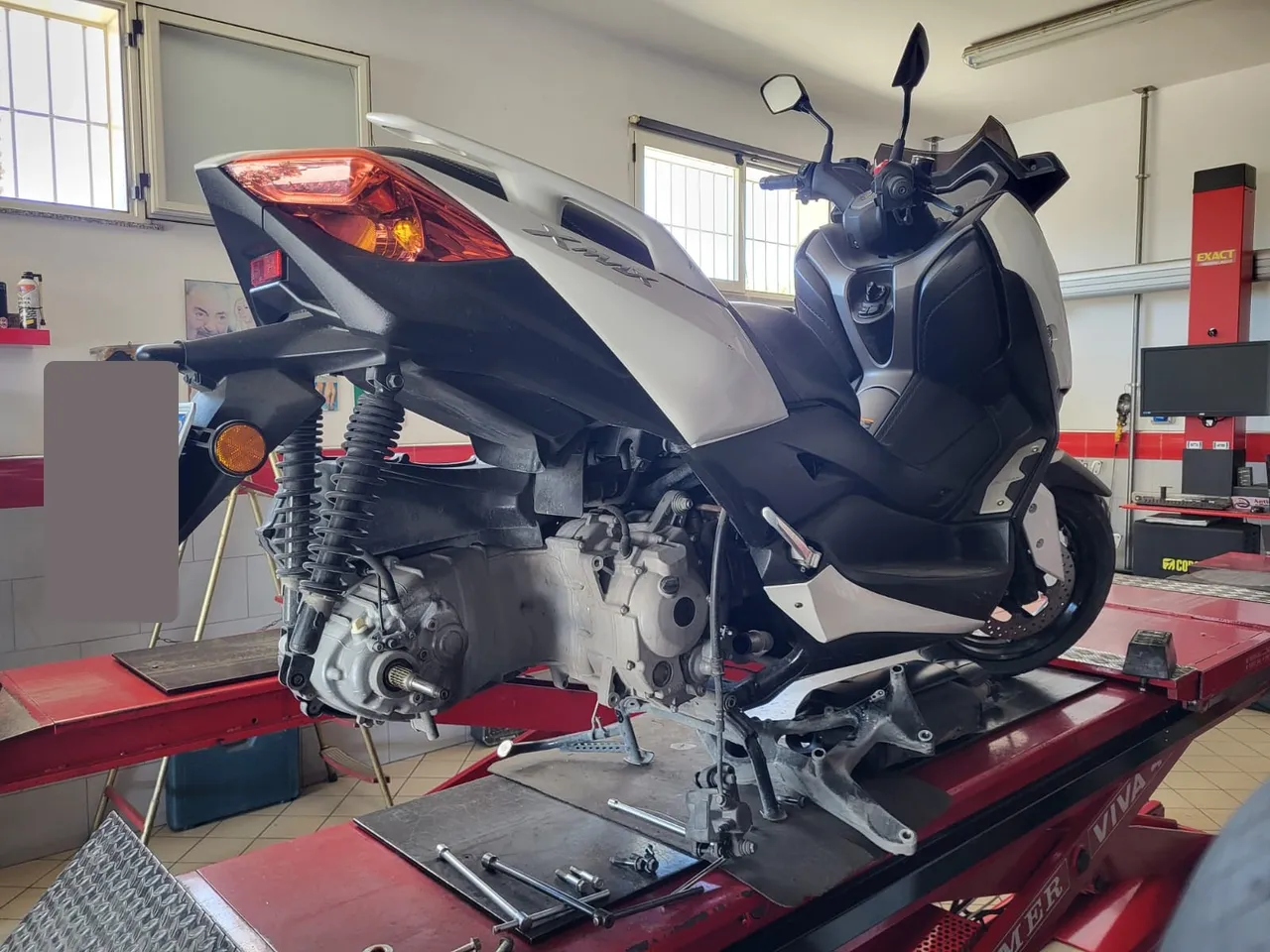Scooter sul ponte con ruota posteriore smontata: accesso libero a gomma, disco e trasmissione.